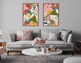 Two framed canvases with colorful floral artwork hung above a light gray sofa with textured cushions in a modern living room setting.