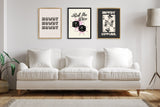 Three framed canvas prints with Western designs hang above a white three-seat sofa, featuring beige and black tones and a floor lamp on the right side.