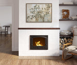 White brick fireplace with a dark metal door containing a burning fire, topped with a wooden mantel and an abstract olive tree painting in muted greens and browns.