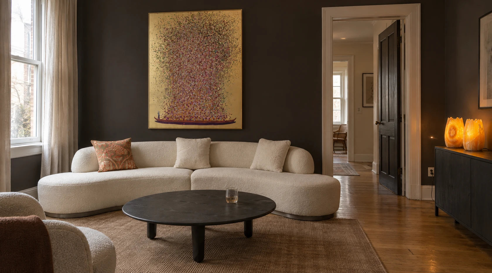 A charcoal room with the Perla curved sofa, Flower Boat artwork, Luna table, embroidered fish pillow and amber onyx lamps.