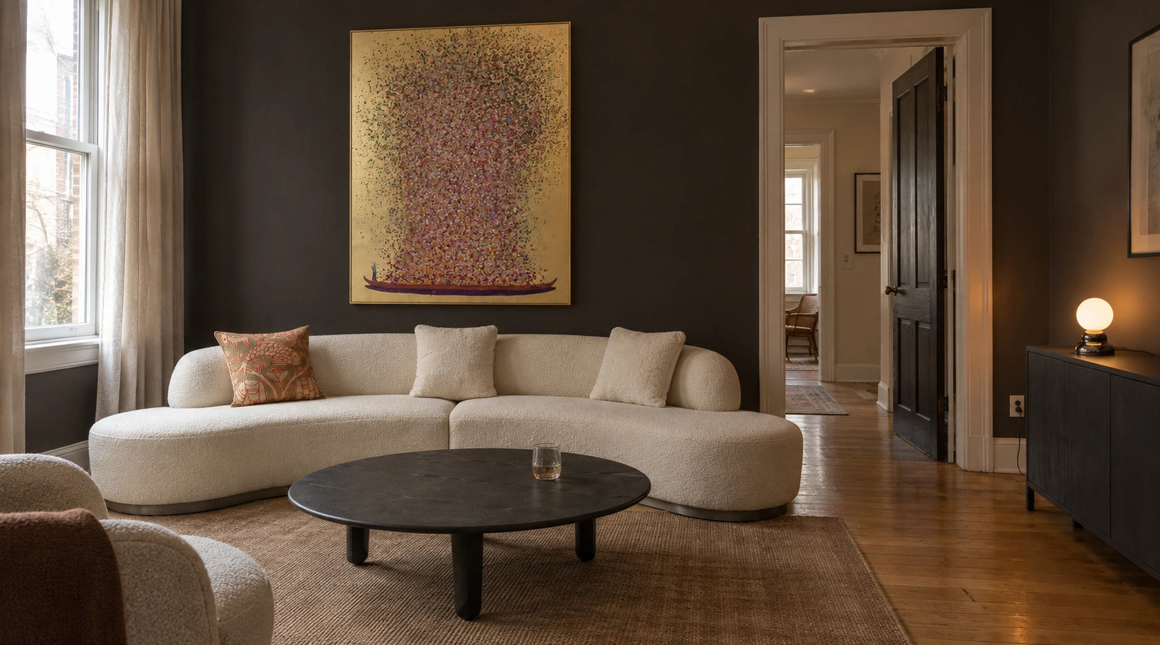 A charcoal living room with the Perla curved sofa, Flower Boat artwork, Luna coffee table, embroidered fish pillow and Ripple II globe lamp.